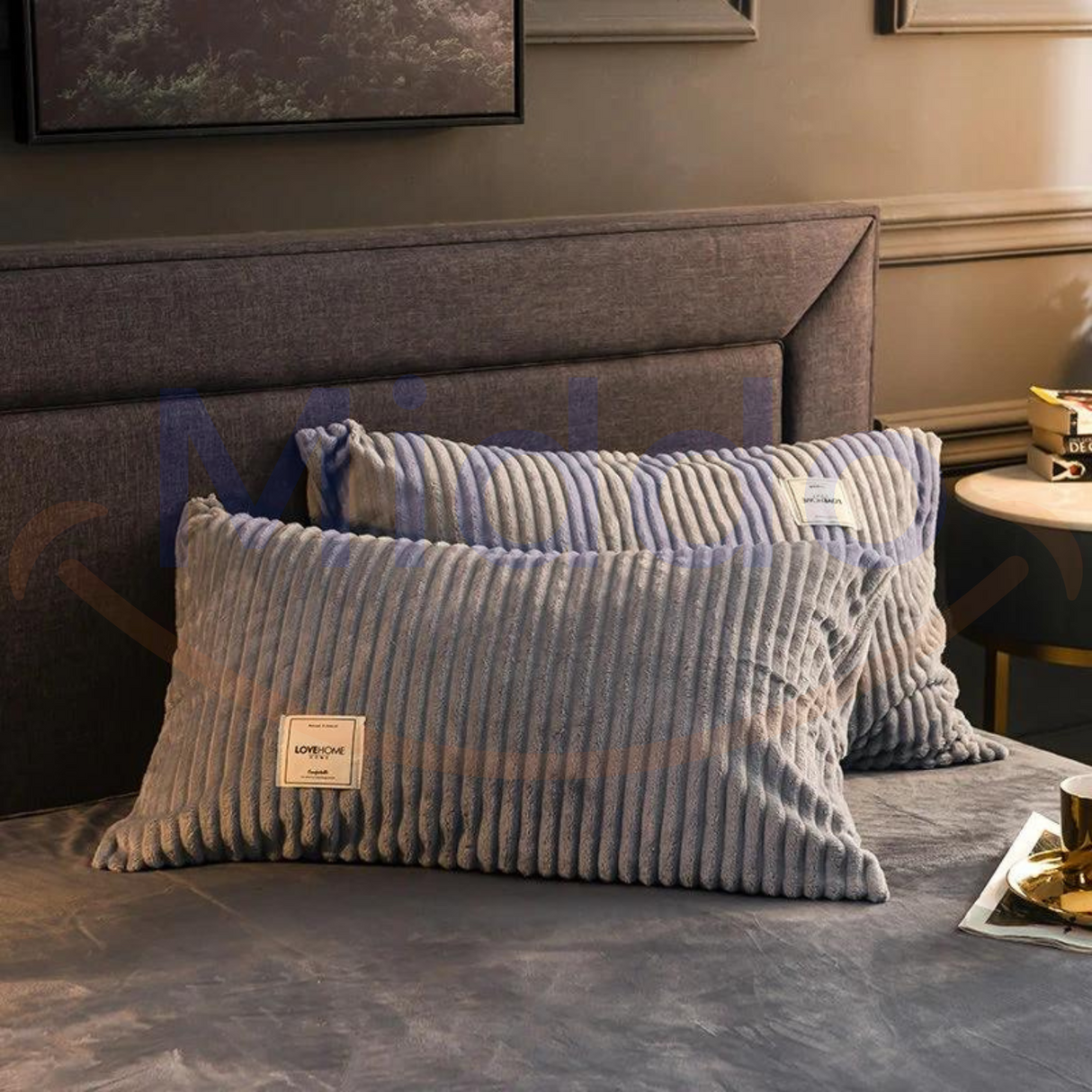 Grijze fluwelen fleece kussens op bed met donkere achtergrond.