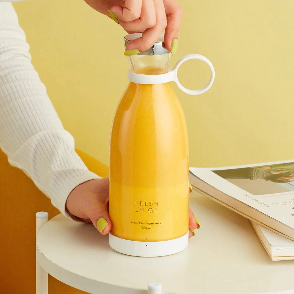 Hand die een draadloze blender met sinaasappelsap gebruikt.