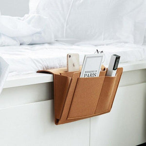 Foto van de bruin lederen BedCaddy hangend aan een wit bed met spullen erin.