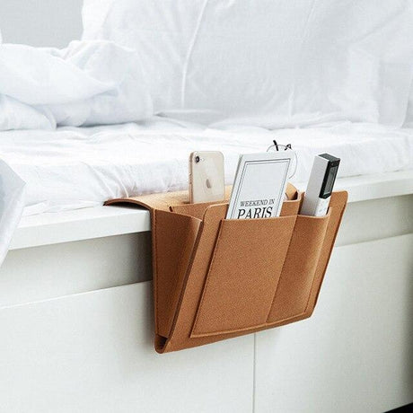 Foto van de bruin lederen BedCaddy hangend aan een wit bed met spullen erin.