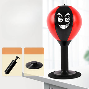 Rood met zwarte FunPunch boksbal met lachend monstergezicht op een standaard met zuignap op een bureaublad, met de meegeleverde pomp en voet ernaast