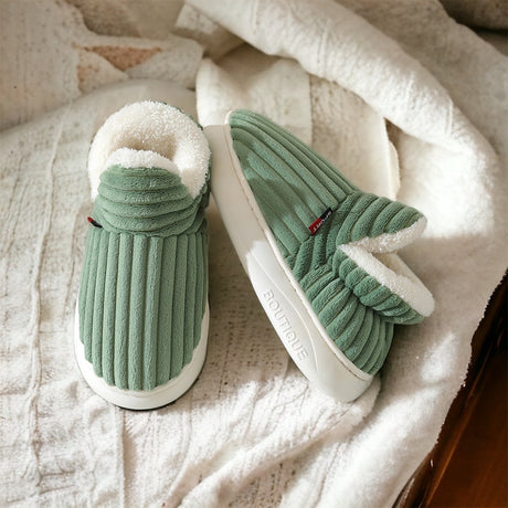 Groene fleece pantoffels met witte fleece voering liggend op een witte zachte deken.