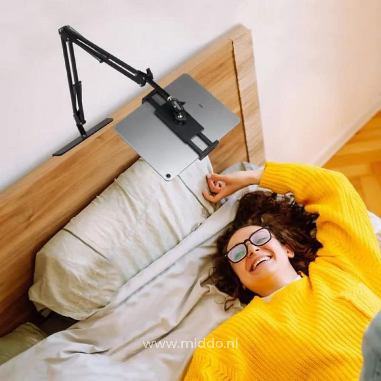 Vrouw ligt in bed met FlexArm tablethouder die aan het hoofdeinde van het bed is bevestigd