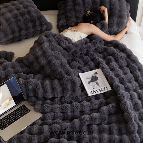 Zwarte Fluffy Toscaanse winterdeken op bed met tijdschrift en laptop