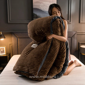 Vrouw op bed die een bruin fluwelen fleece dekbedovertrek met ribstructuur en donkere bies tegen zich aan houdt