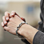 Persoon met gevouwen handen draagt een zilveren drakenarmband, buiten gefotografeerd