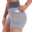 Zijaanzicht van een vrouw in een grijs-witte FlexFit yoga short met wafelstructuur en hoge taille, die een telefoon in het zijzakje steekt