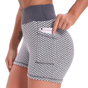 Zijaanzicht van een vrouw in een grijs-witte FlexFit yoga short met wafelstructuur en hoge taille, die een telefoon in het zijzakje steekt