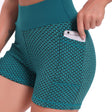 Zijaanzicht van een vrouw in een petrolgroene FlexFit yoga short met wafelstructuur en hoge taille, die een telefoon in het zijzakje steekt