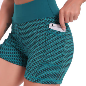 Zijaanzicht van een vrouw in een petrolgroene FlexFit yoga short met wafelstructuur en hoge taille, die een telefoon in het zijzakje steekt