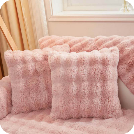 Roze pluche kussens en deken op een bank bij een raam