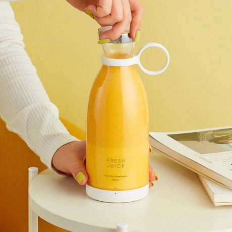 Hand die een draadloze blender met sinaasappelsap gebruikt.